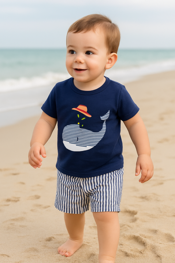 Toddler summer outfit featuring a navy blue- t-shirt with a white- striped whale graphic wearing a red hat and water spout detail, paired with white and navy vertical striped shorts.